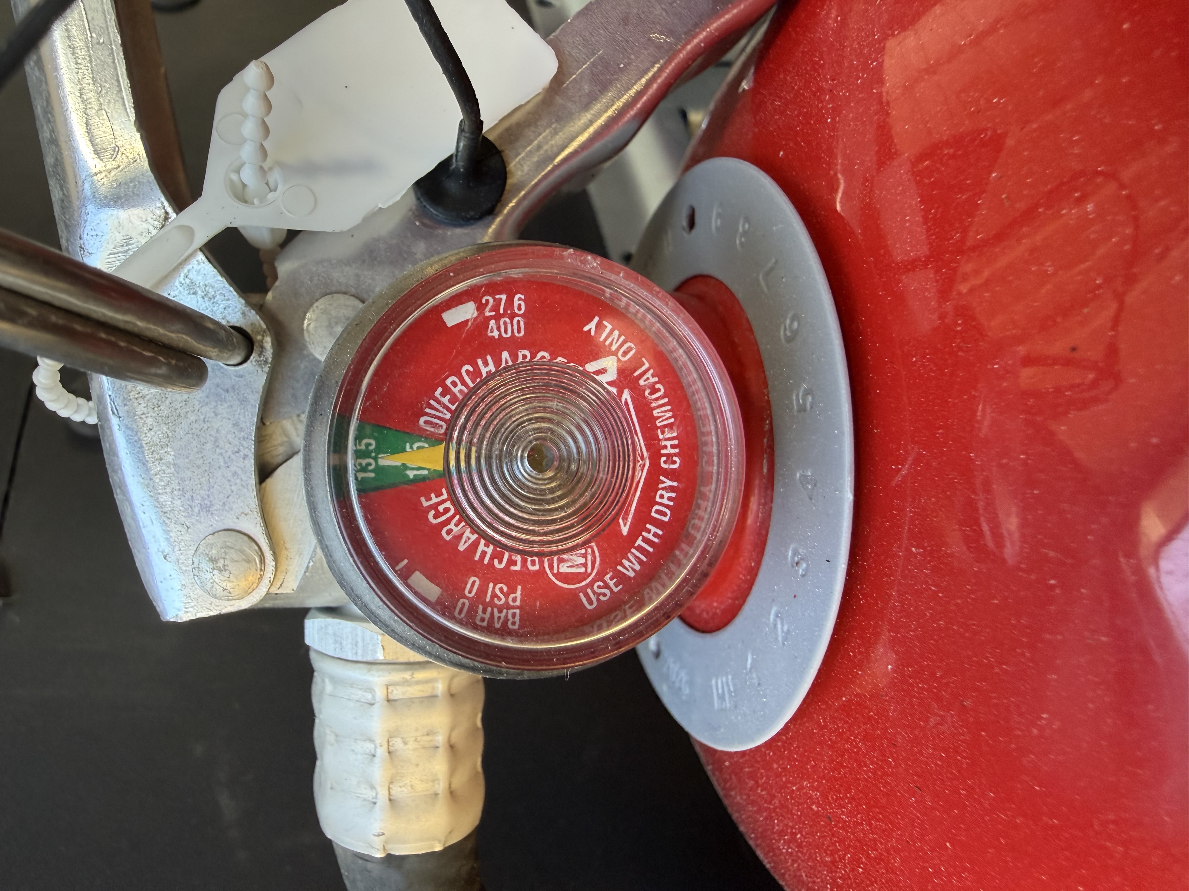 A close-up of the inspection tag hanging from a wall-mounted extinguisher in a commercial space.