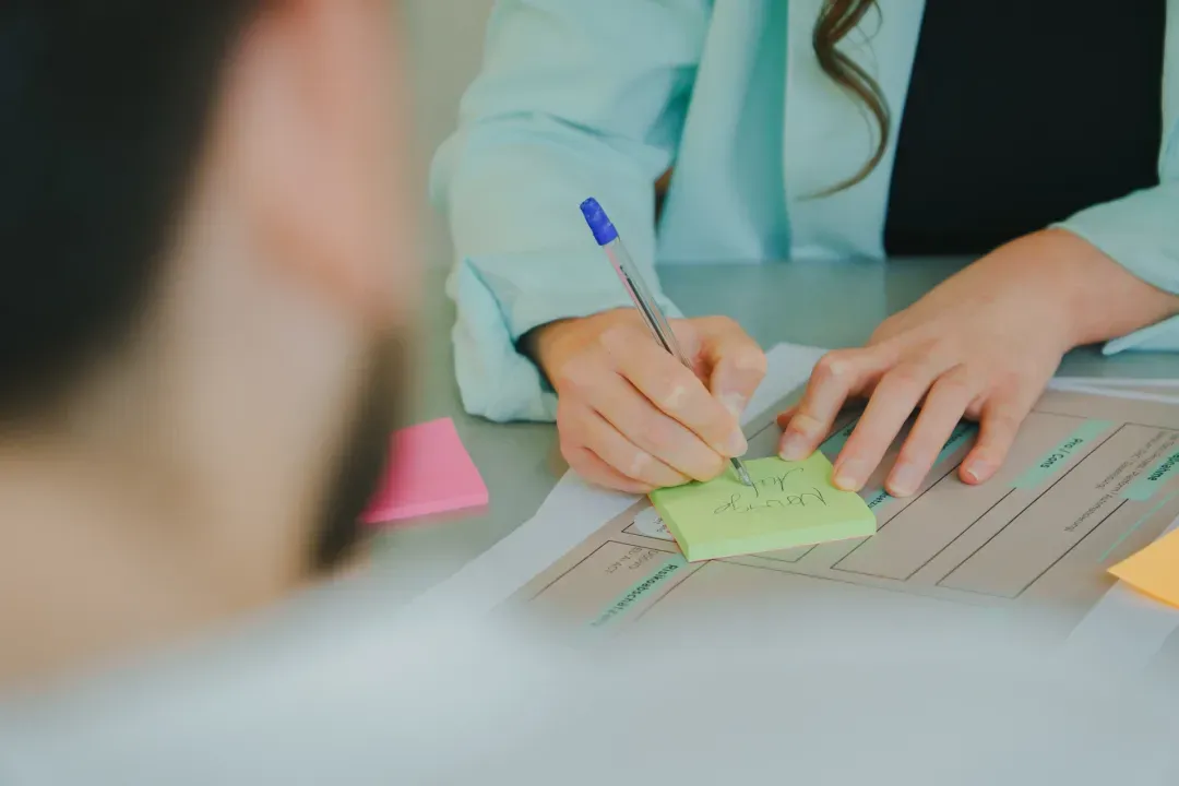Hände mit Stift und Haftnotizen auf einem Arbeitstisch