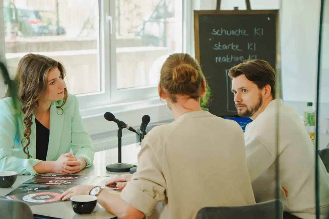 Workshop am Tisch mit Mikrofonen und Tafel, auf der Stärken und Schwächen von KI gesammelt sind