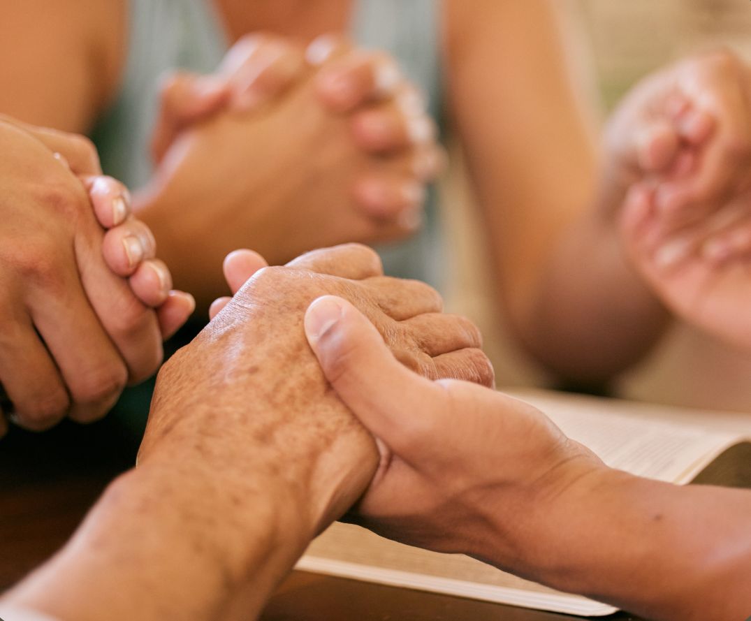 Hands joined in prayer over an open Bible