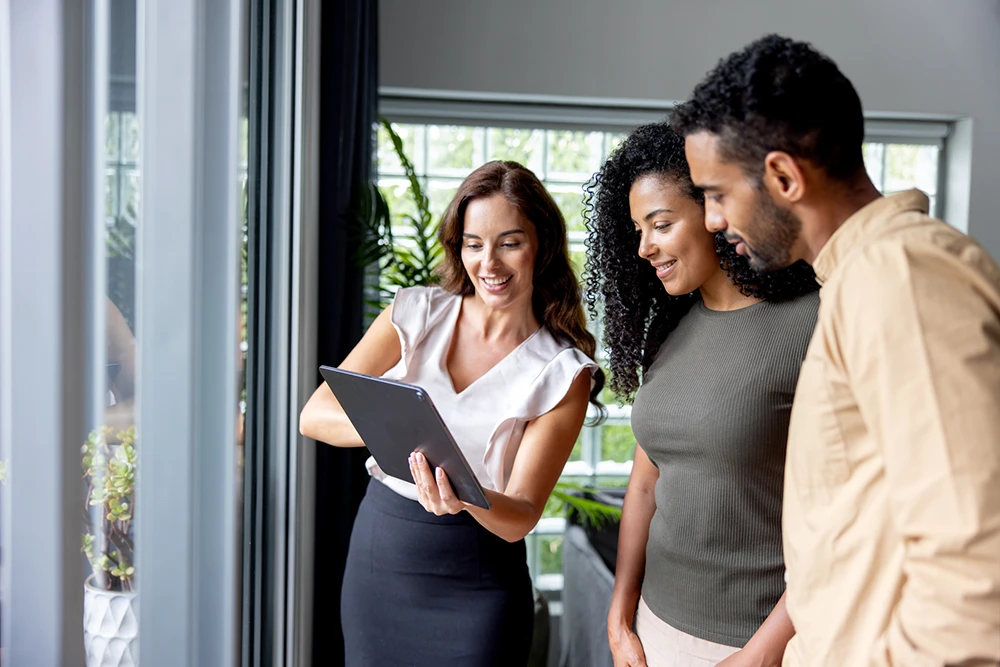 property manager showing two young clients something on her tablet while standing in their clients new home