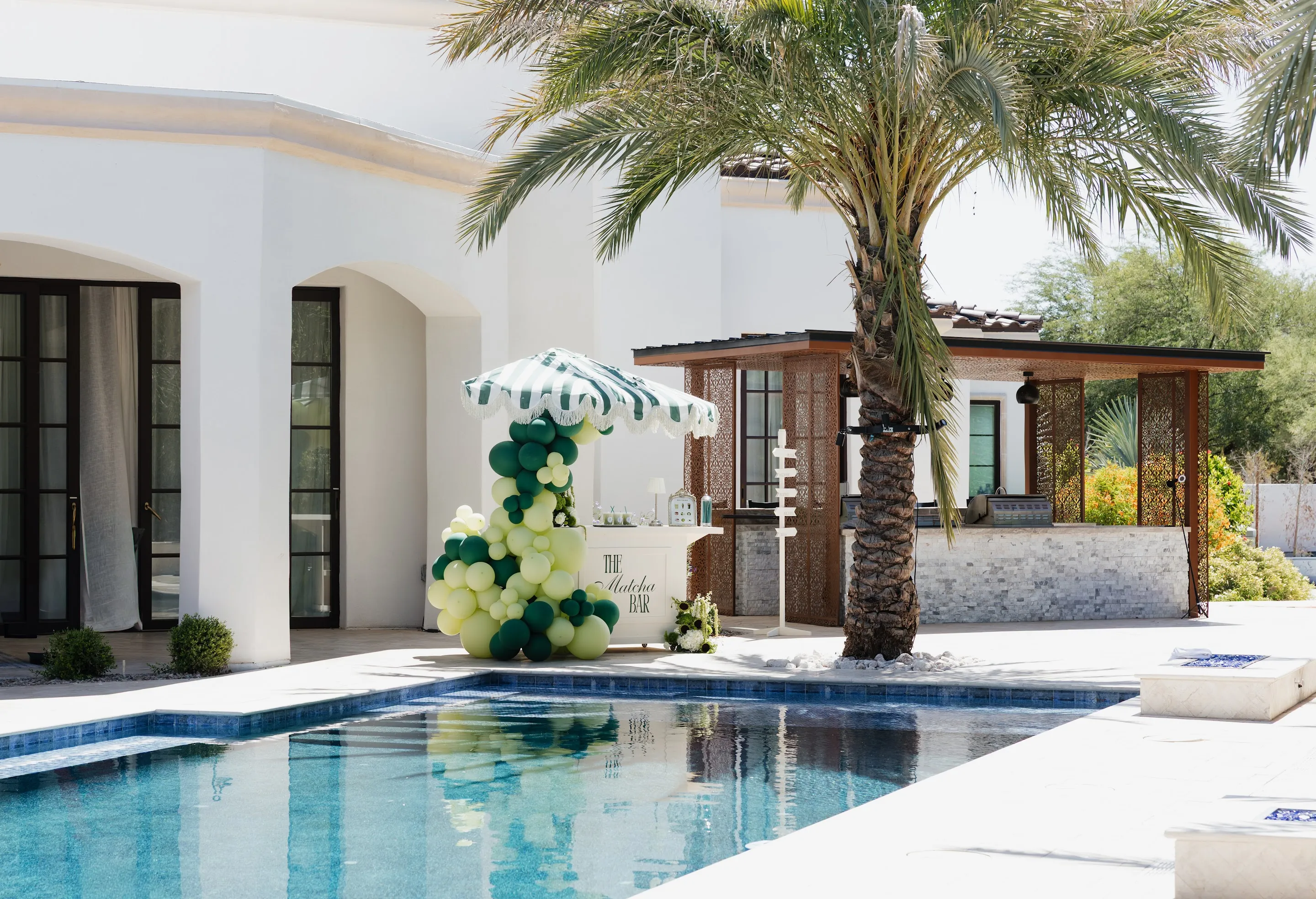 The Matcha Bar cart with a striped umbrella and balloon garland beside a pool