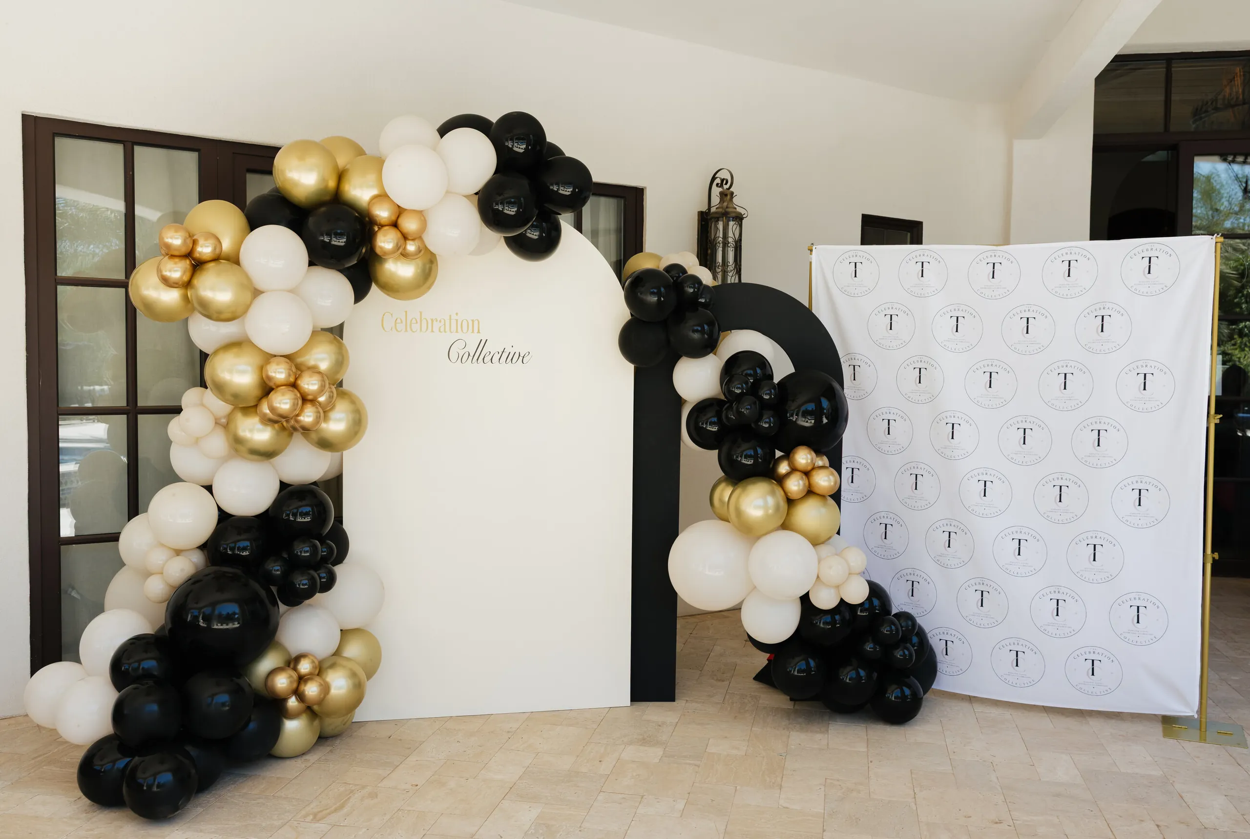 Black, gold and cream balloon arch beside a monogram step-and-repeat wall