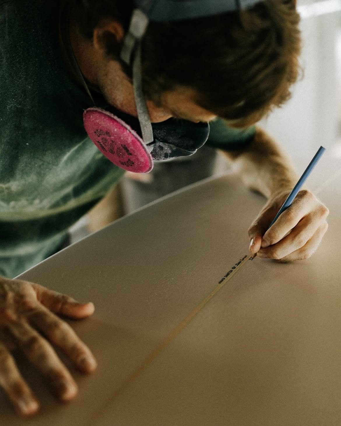 Person wearing a dust mask carefully working with a tool on a smooth surface, focusing on precise detailing.