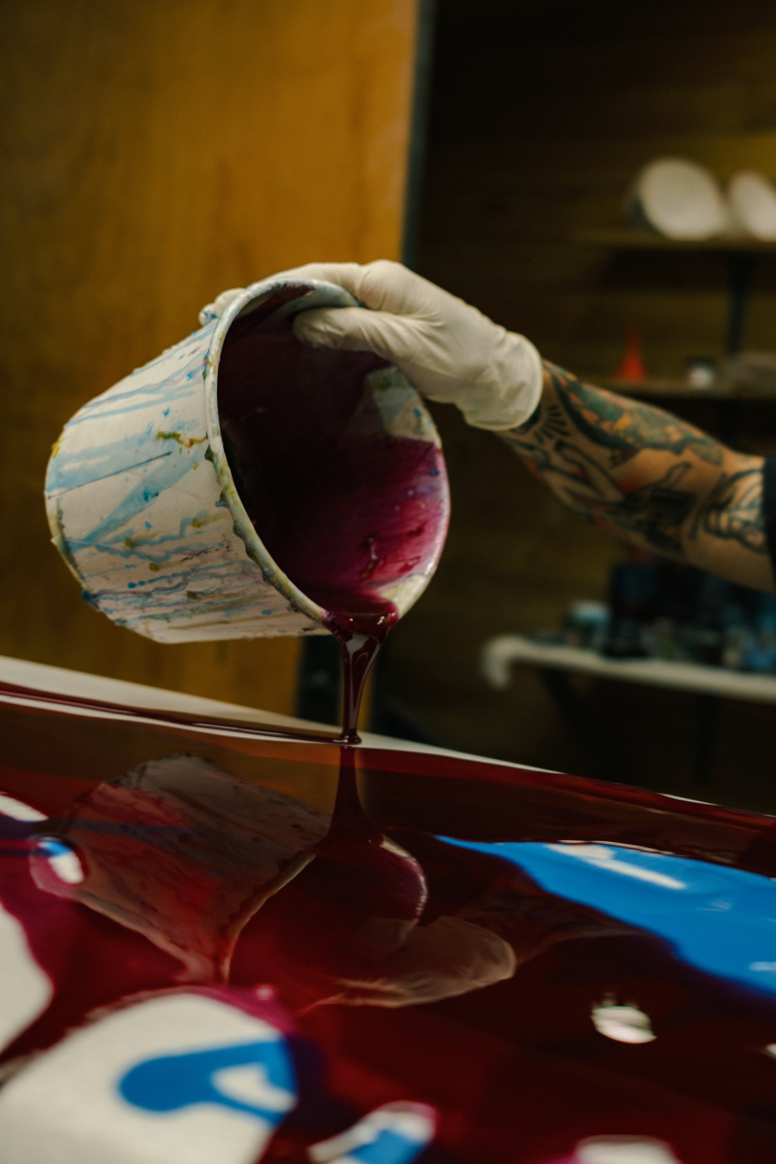 Pouring tinted resin onto a surfboard during glassing at House of Somos