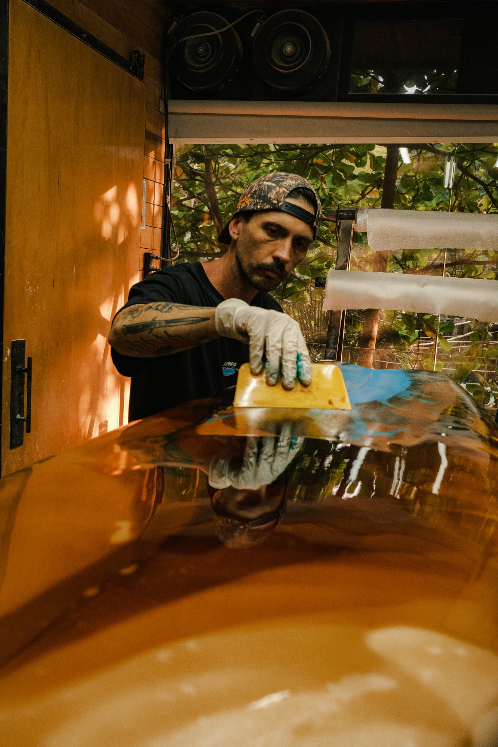 Smoothing a freshly glassed orange surfboard in the workshop