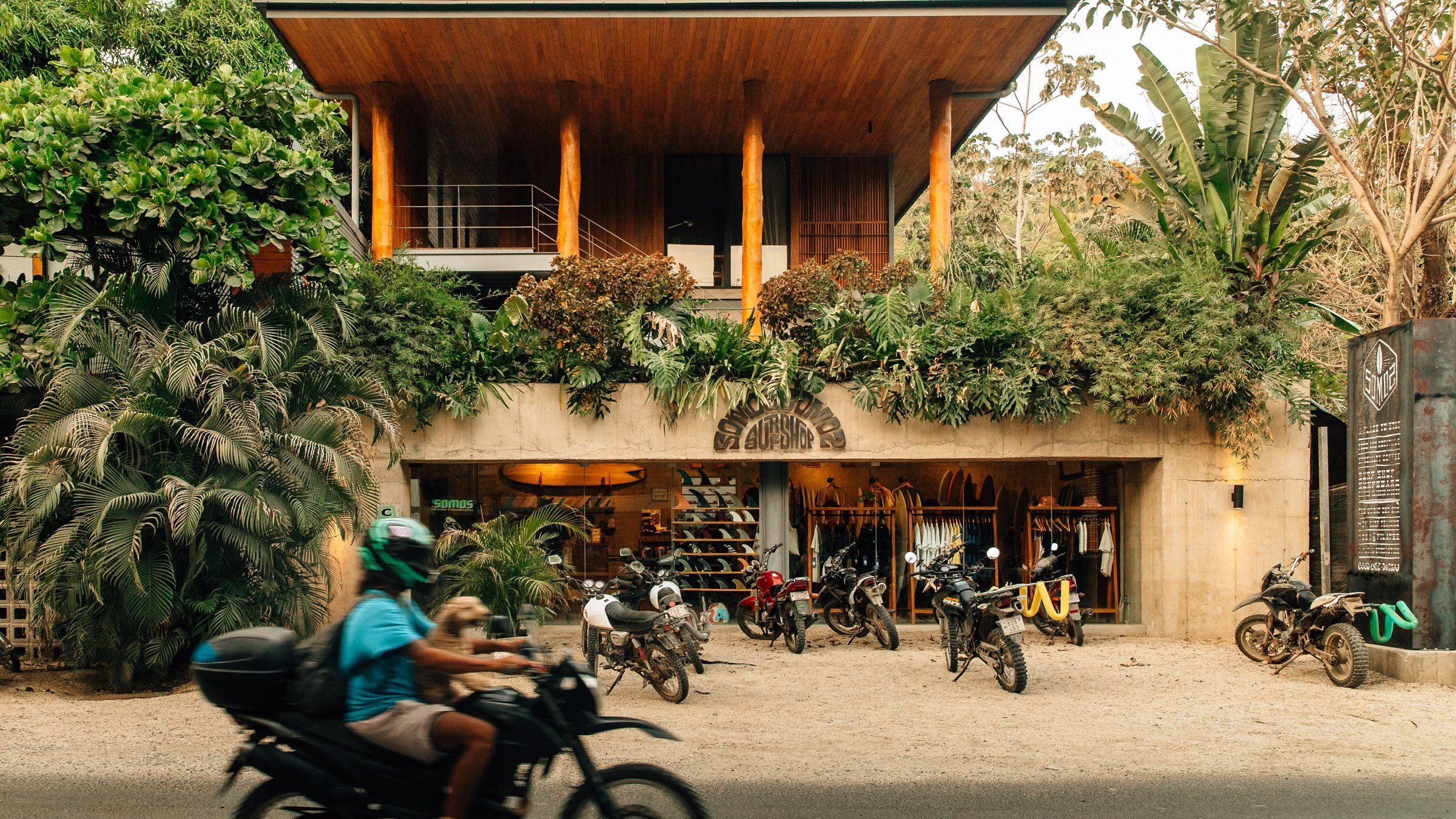 The House of Somos building in Santa Teresa, with motorbikes parked out front and a rider passing on the road.