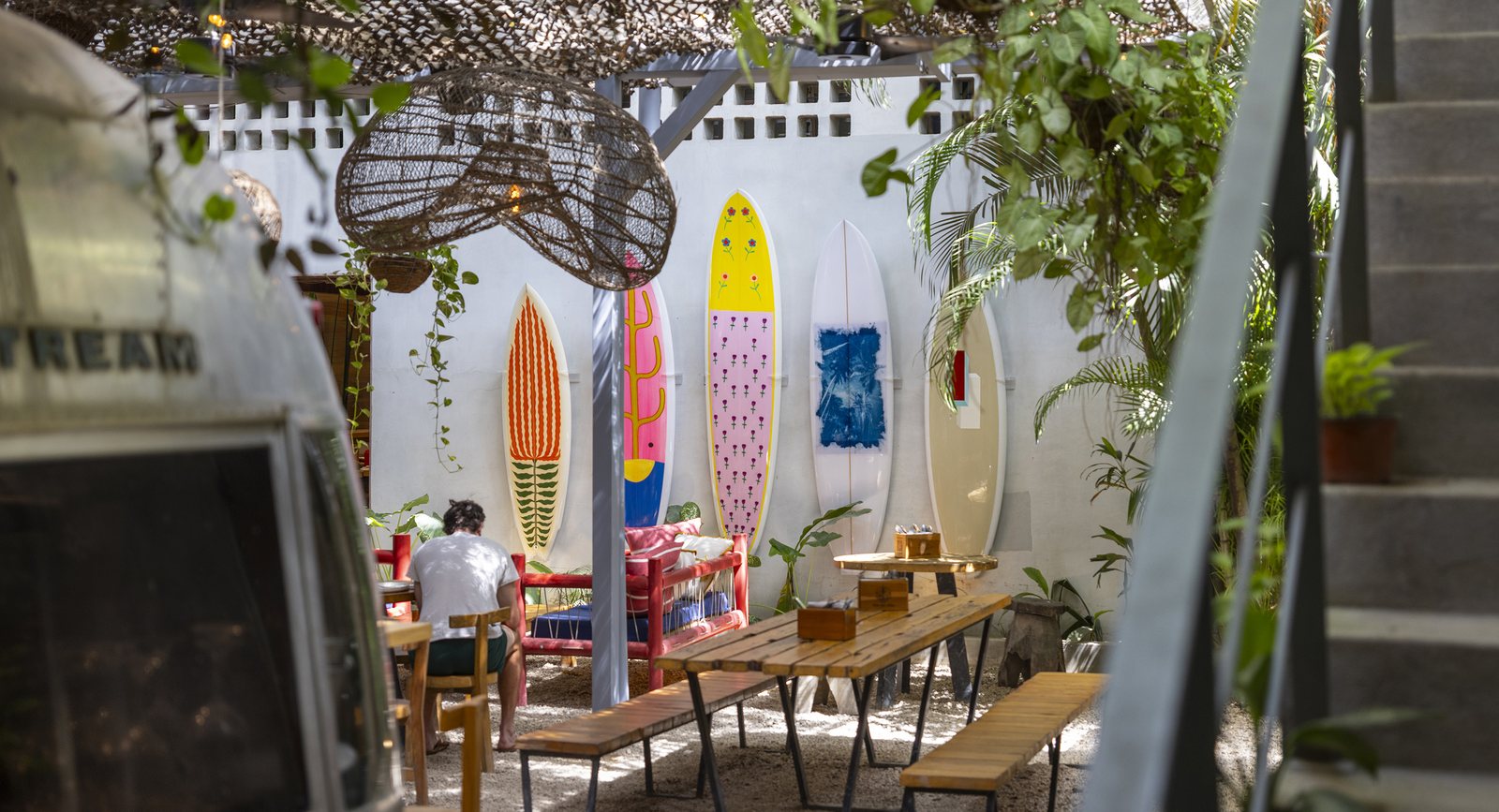 The House of Somos café courtyard with a vintage Airstream, wooden tables, hanging woven lamps and painted surfboards along the wall.