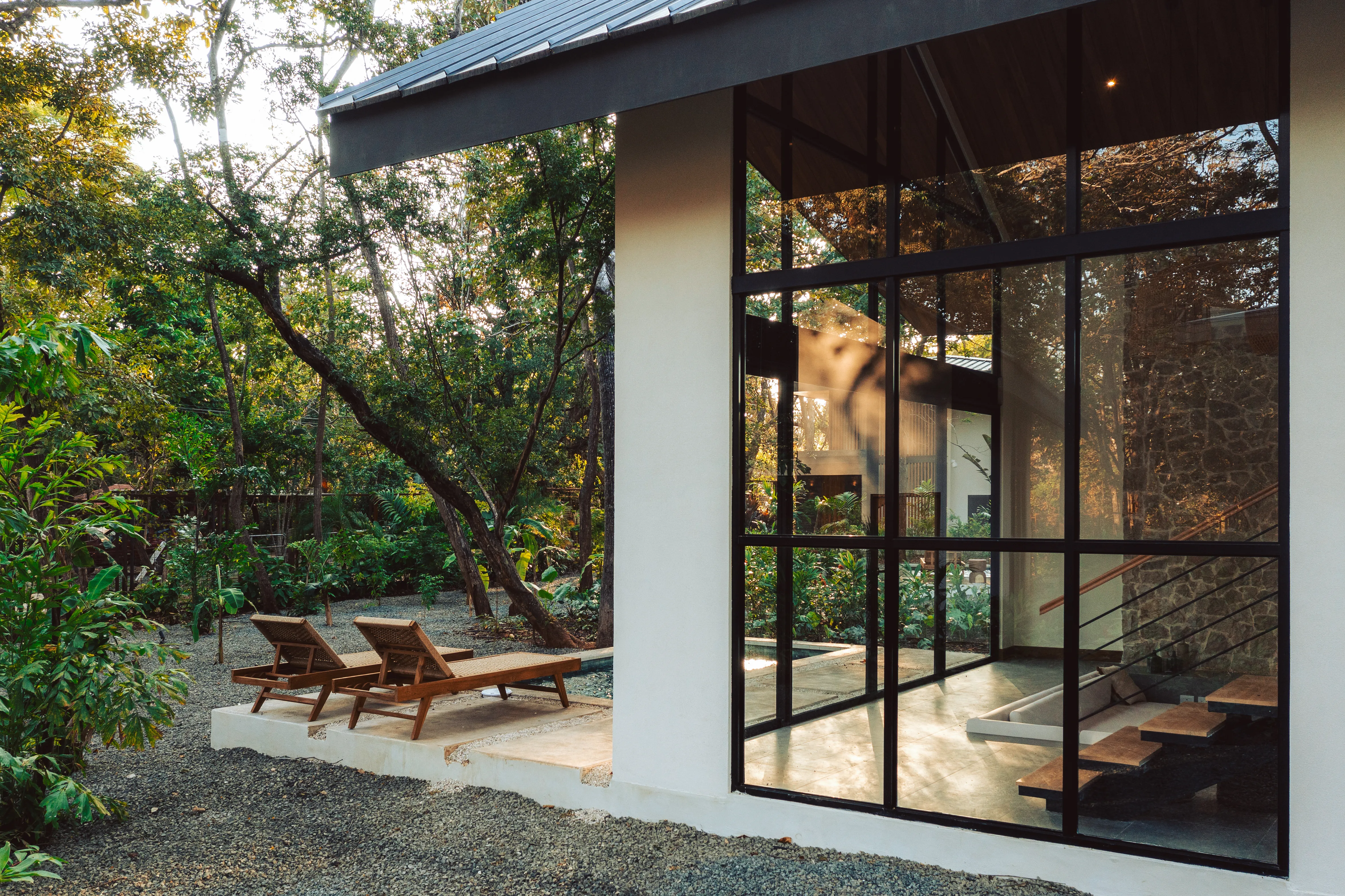 Somos Pool Villa 1BR: glass-walled villa with two lounge chairs on the terrace among the trees