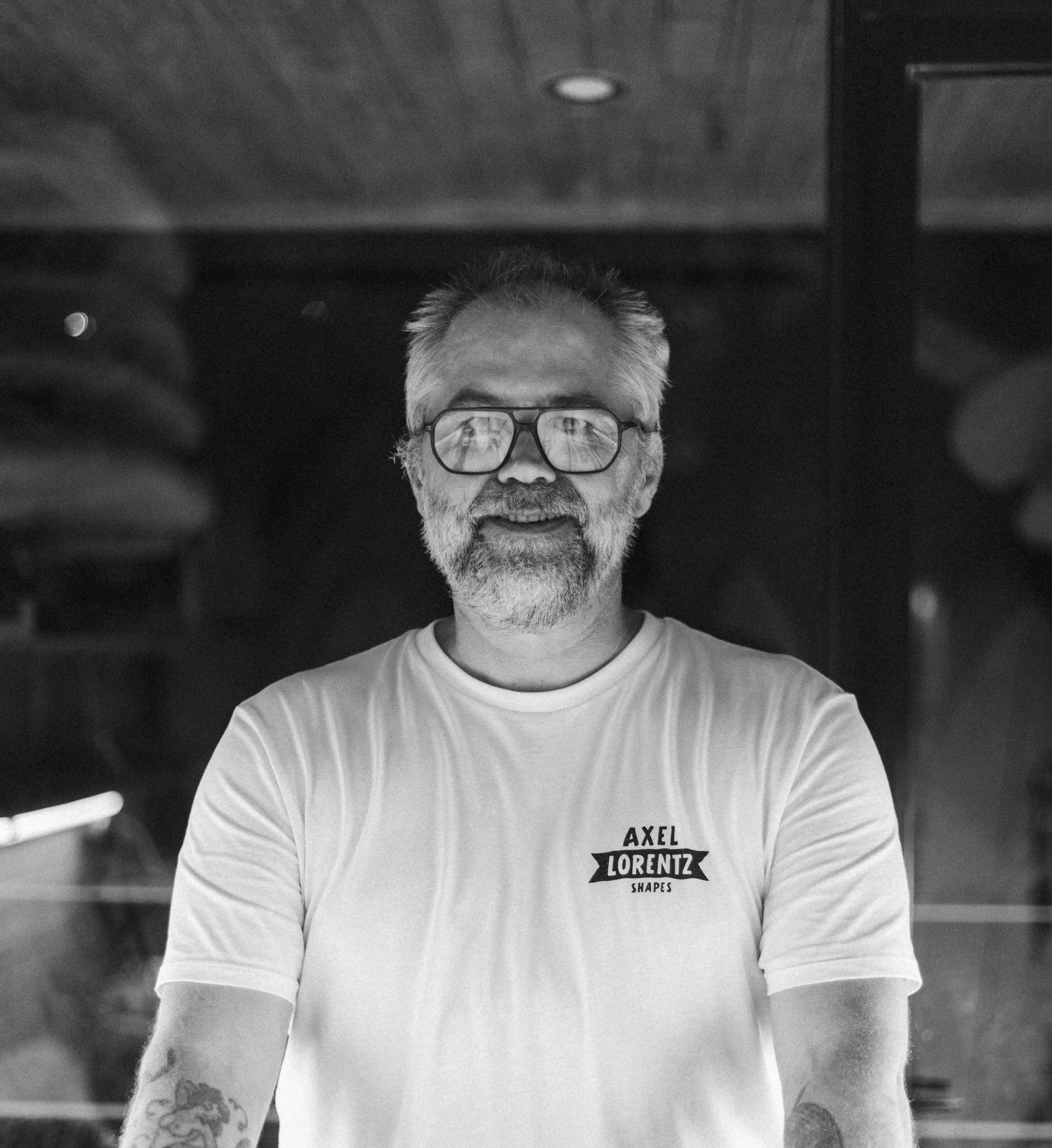 Black-and-white portrait of a shaper standing in a wood-lined workshop.