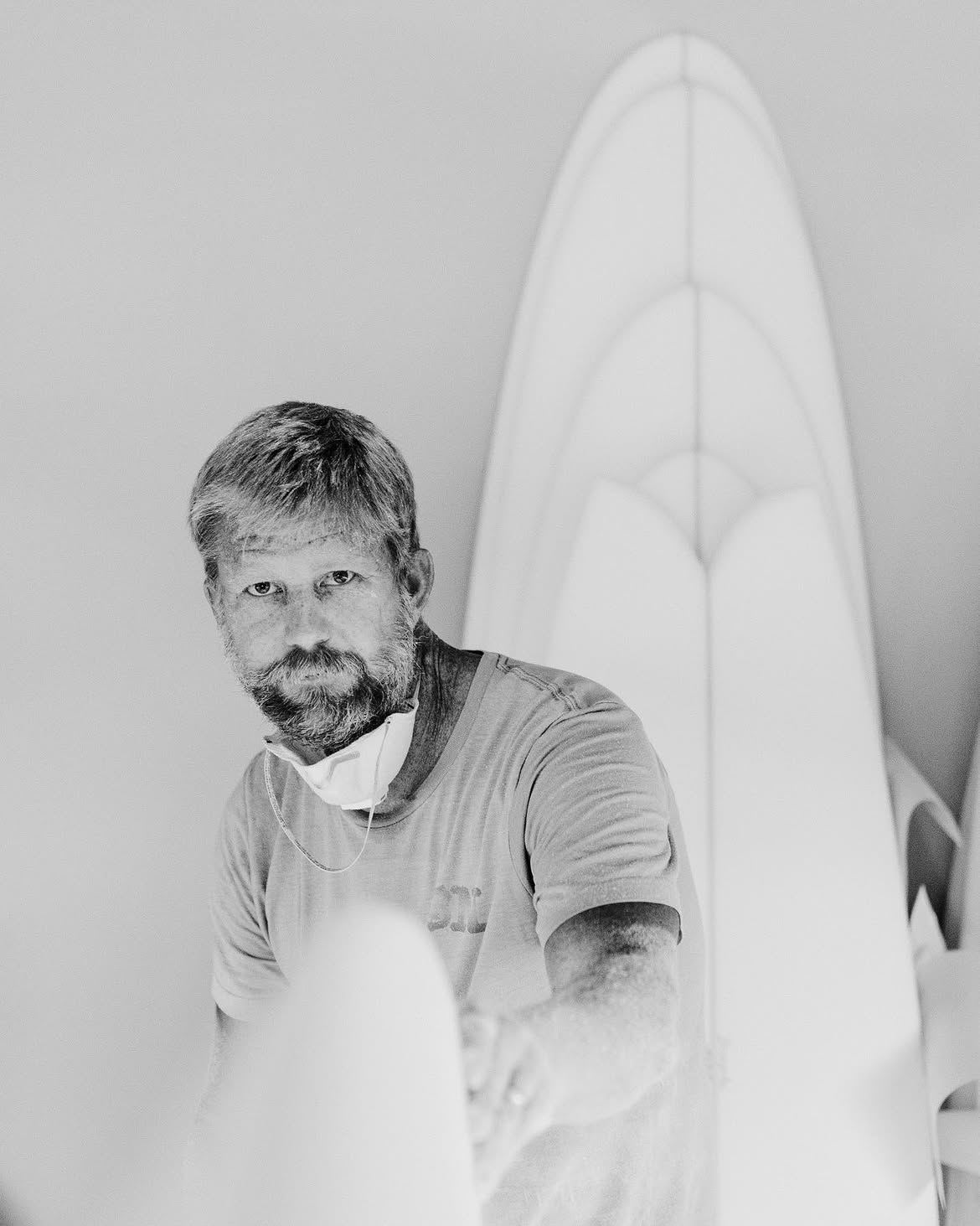 Black-and-white portrait of a shaper beside a surfboard.