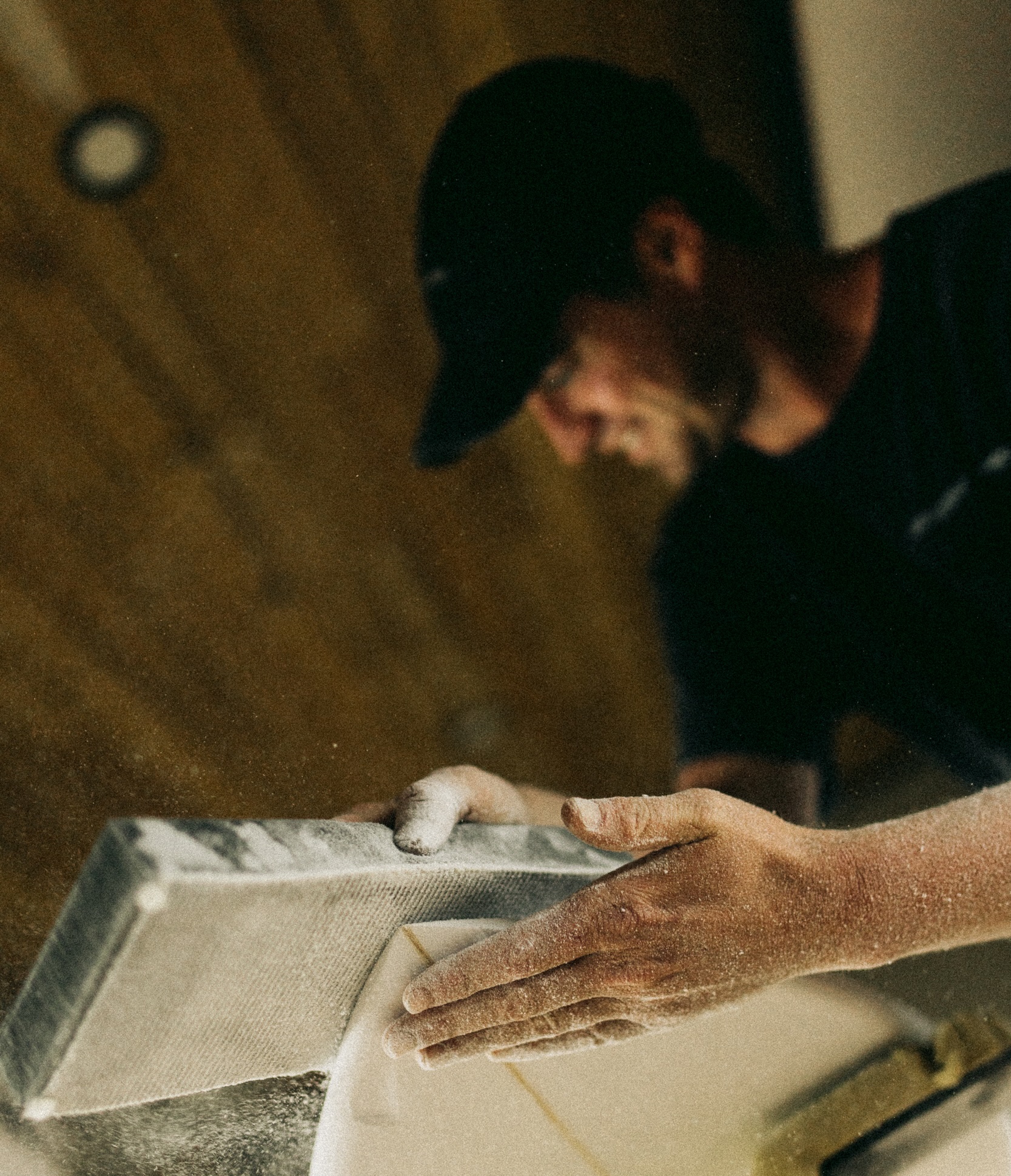 A builder works by hand on a surfboard rail in the shaping bay.