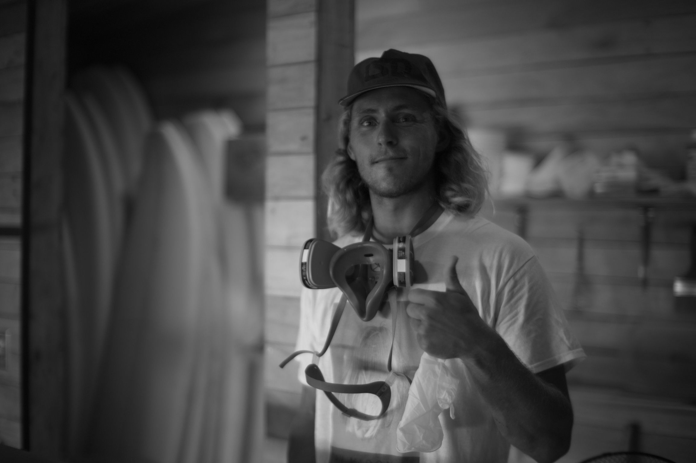 Black-and-white portrait of a masked surfboard builder holding a power tool.
