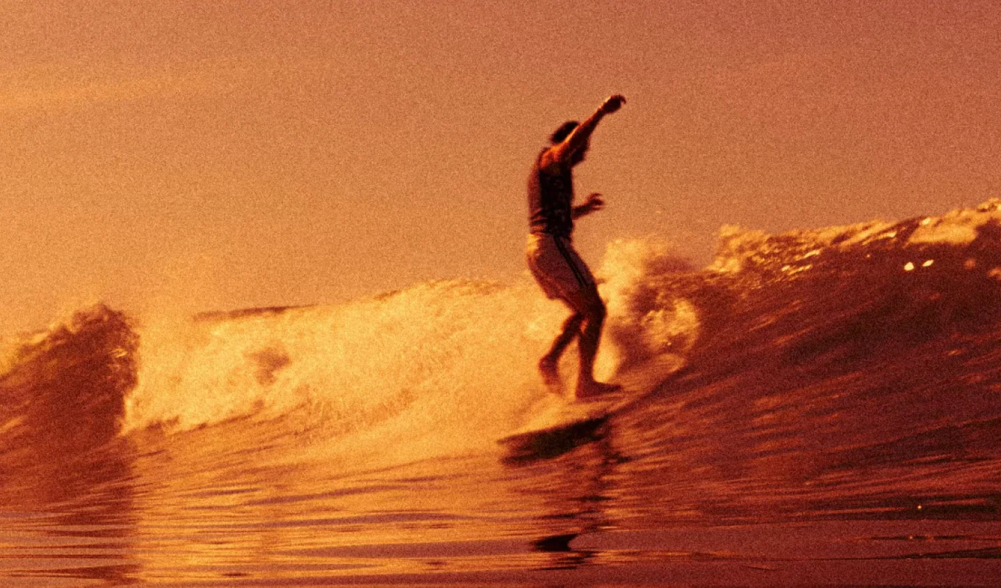 Surfer riding an orange-lit wave