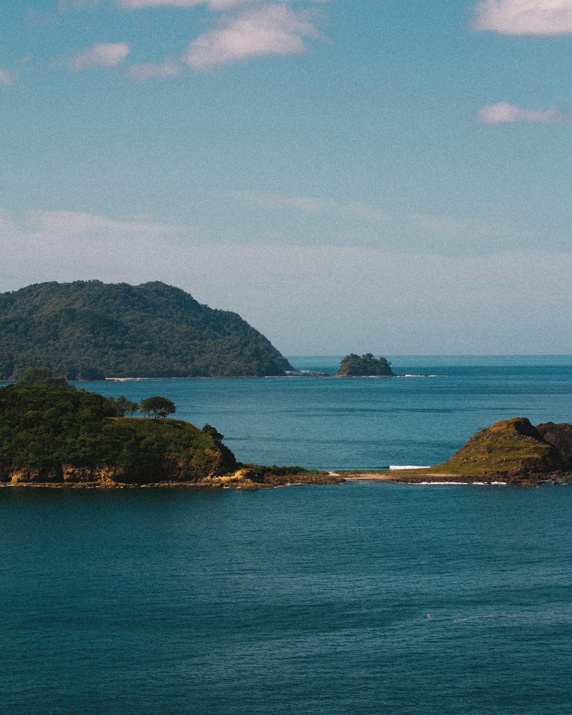 Scenic view of green, tree-covered islands surrounded by calm blue ocean under a partly cloudy sky.