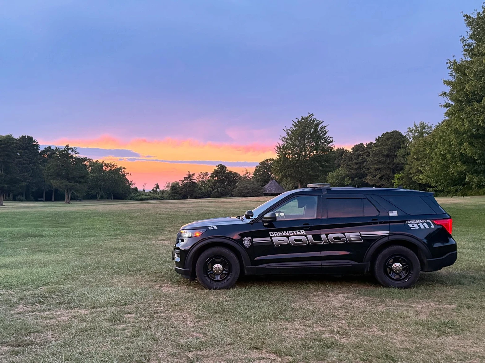 A Brewster Police patrol SUV parked on a grassy field beneath a pink and orange Cape Cod sunset
