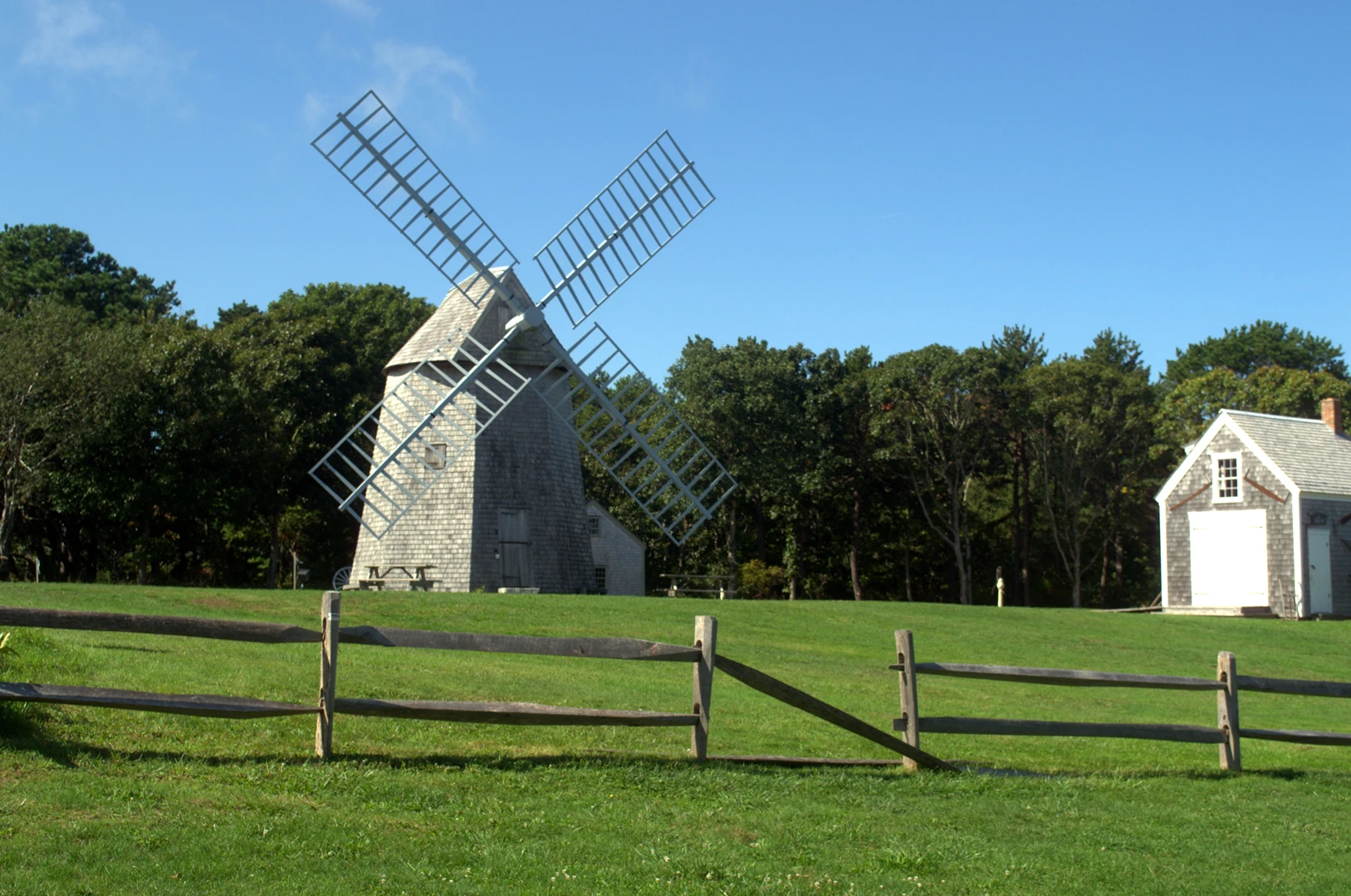 A historic Cape Cod windmill on a green lawn behind a split-rail fence