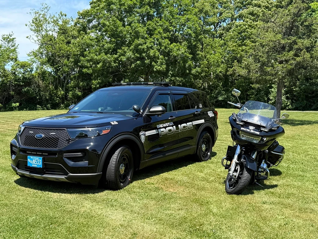 A Brewster Police SUV and police motorcycle parked side by side on a sunlit green field