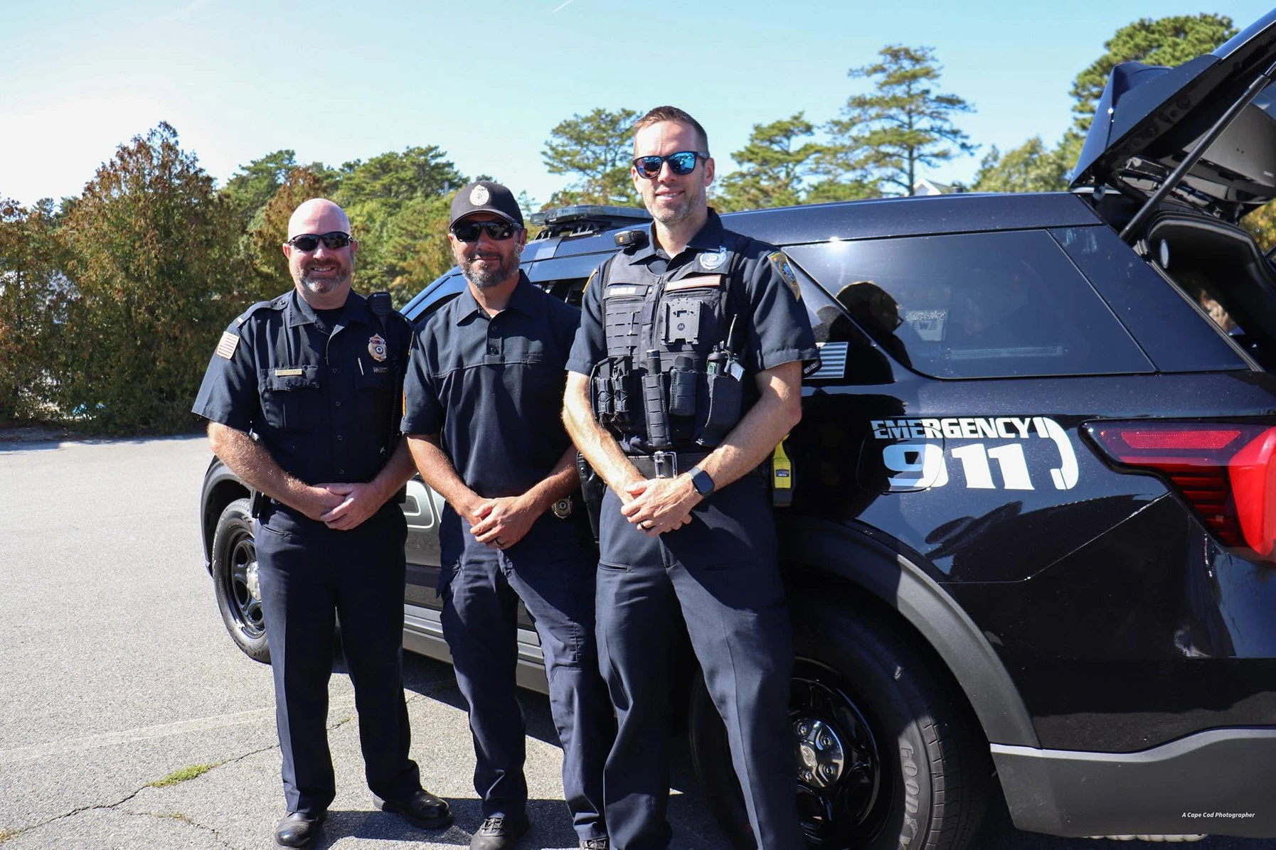 Three Brewster officers standing together beside a patrol SUV on a clear day