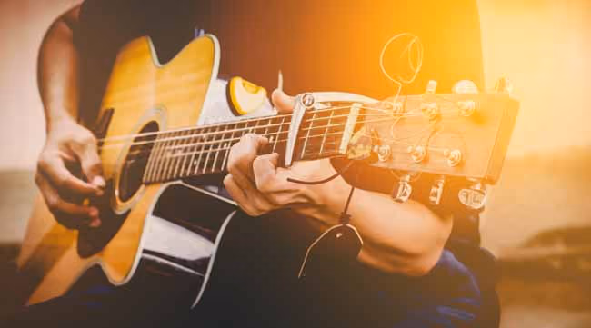 Person playing an acoustic guitar with a capo on the neck, bathed in warm, golden sunlight.