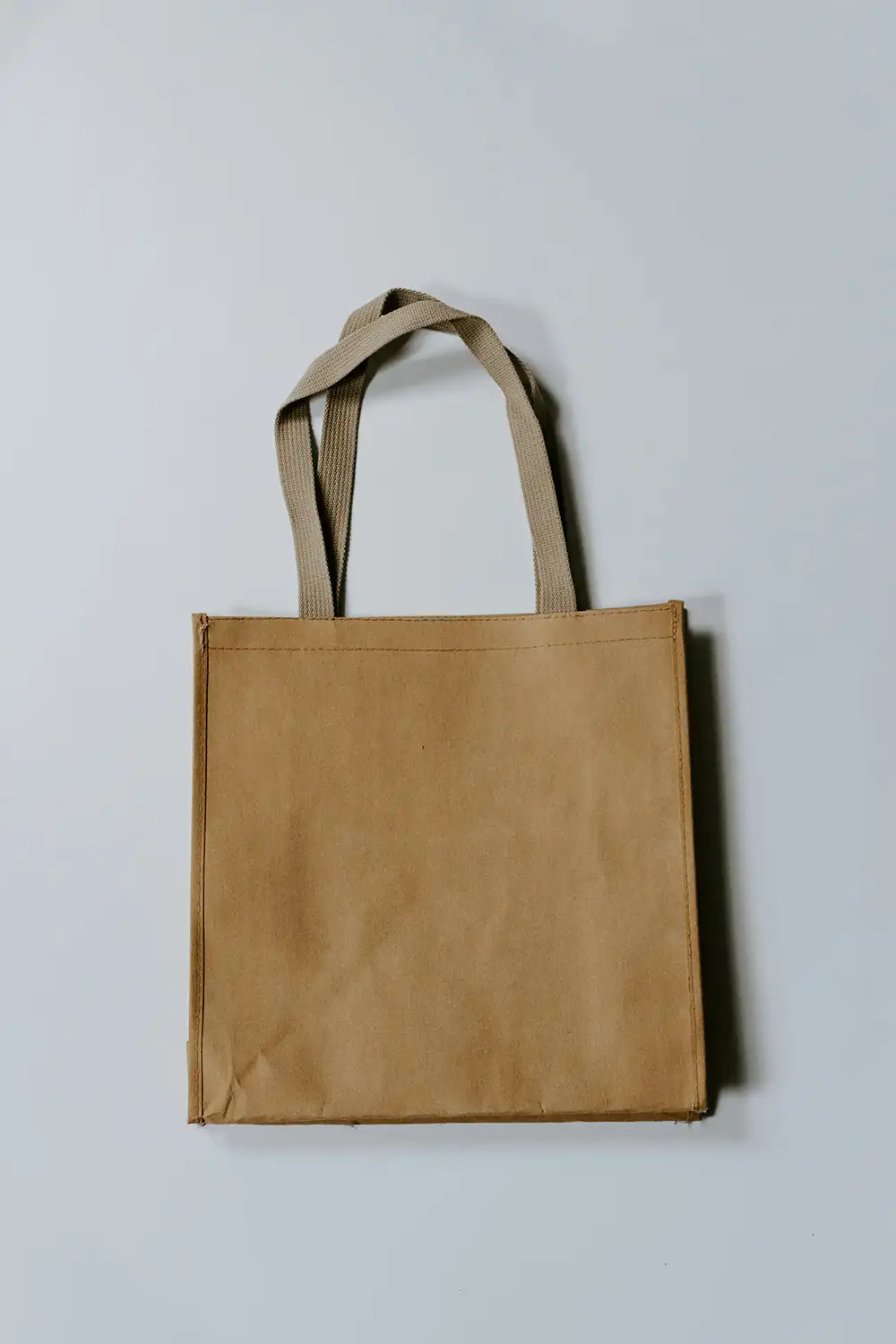 Plain brown reusable tote bag with two fabric handles on a white background.