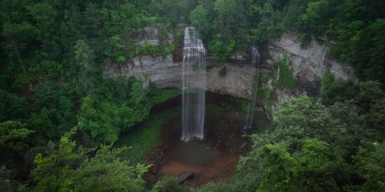 East Tennessee Attractions: A tall waterfall dropping from a clifftop into a green pool at the bottom of a wooded gorge.