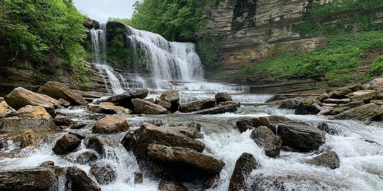 East Tennessee Attractions: A wide waterfall spilling over layered rock ledges into a boulder-strewn river.