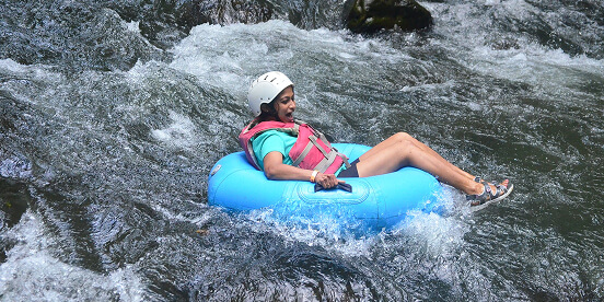 East Tennessee Attractions: A person in a helmet and life vest riding an inner tube down whitewater rapids.