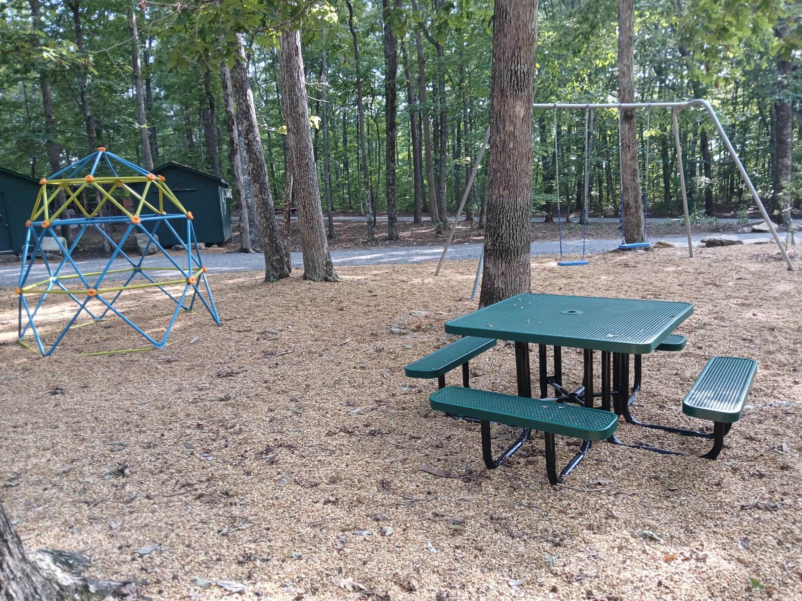 Vacation Rentals in Tennessee: A playground near the campsites with a climbing dome, a swing set, and a teal picnic table on wood chips.