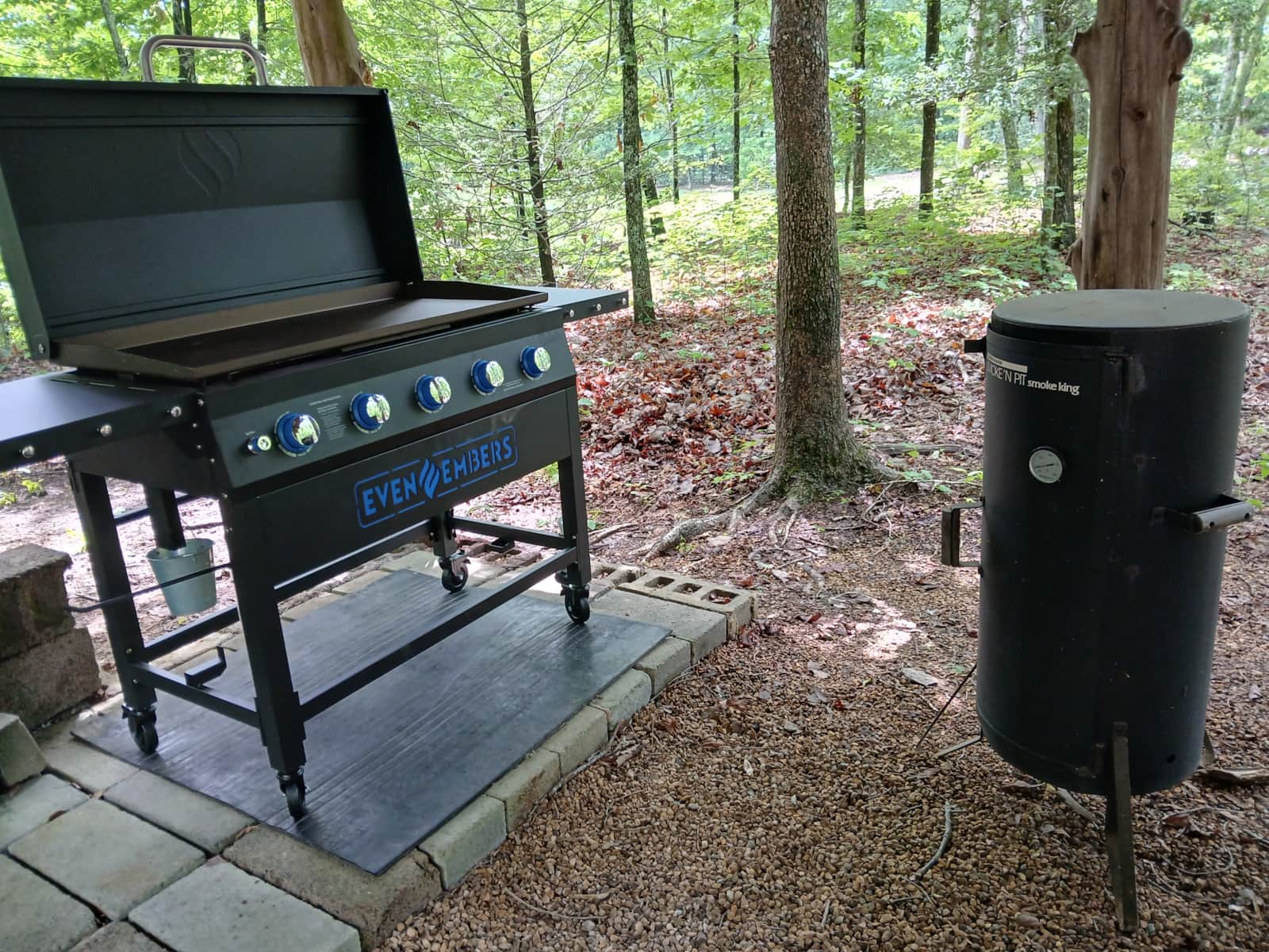 Vacation Rentals in Tennessee: An outdoor flat-top griddle and a barrel smoker set on pavers in the shade of the woods.