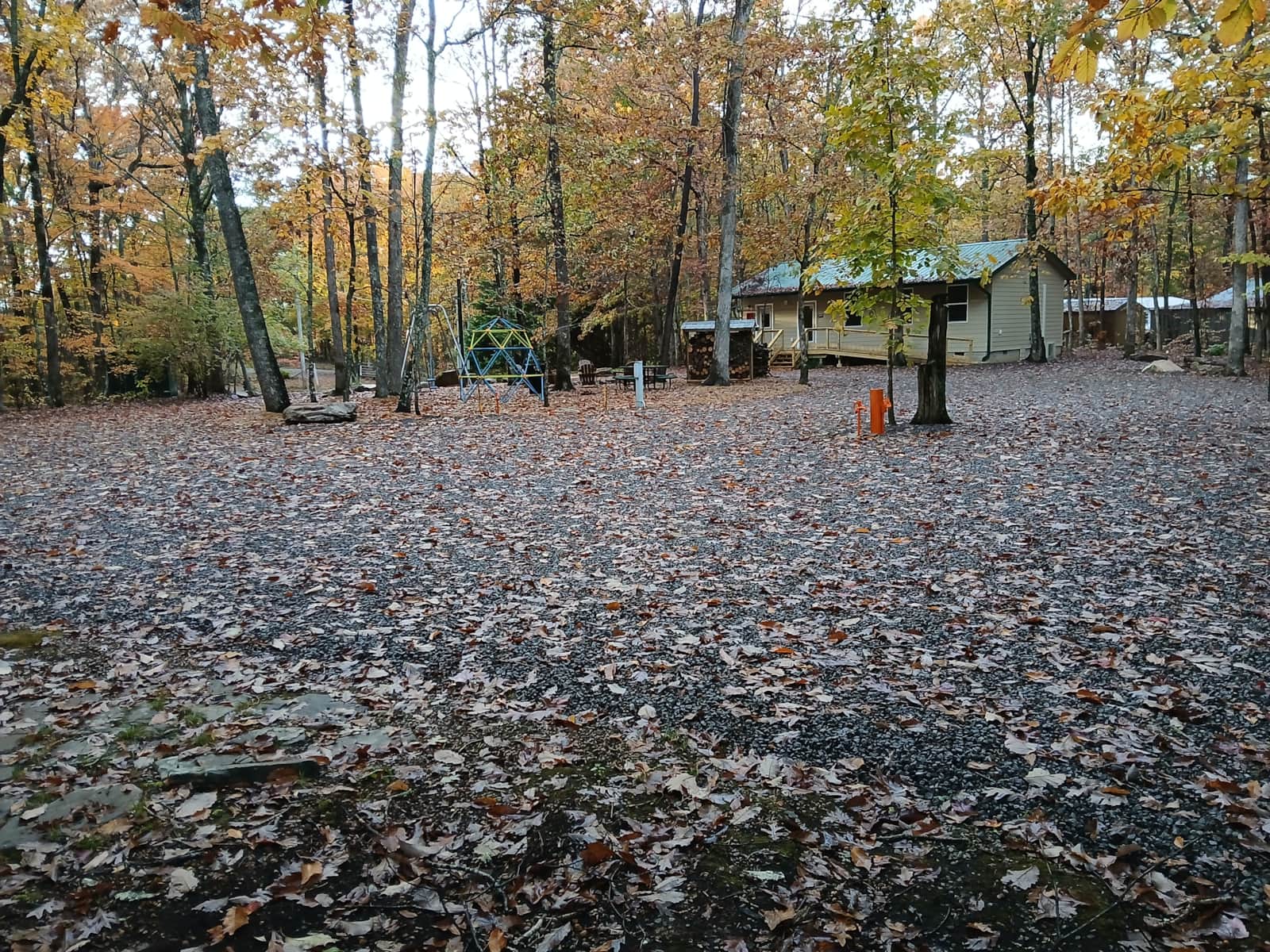 Vacation Rentals in Tennessee: A leaf covered RV site in autumn, with a hookup post in front and a small green roofed shelter in the background.
