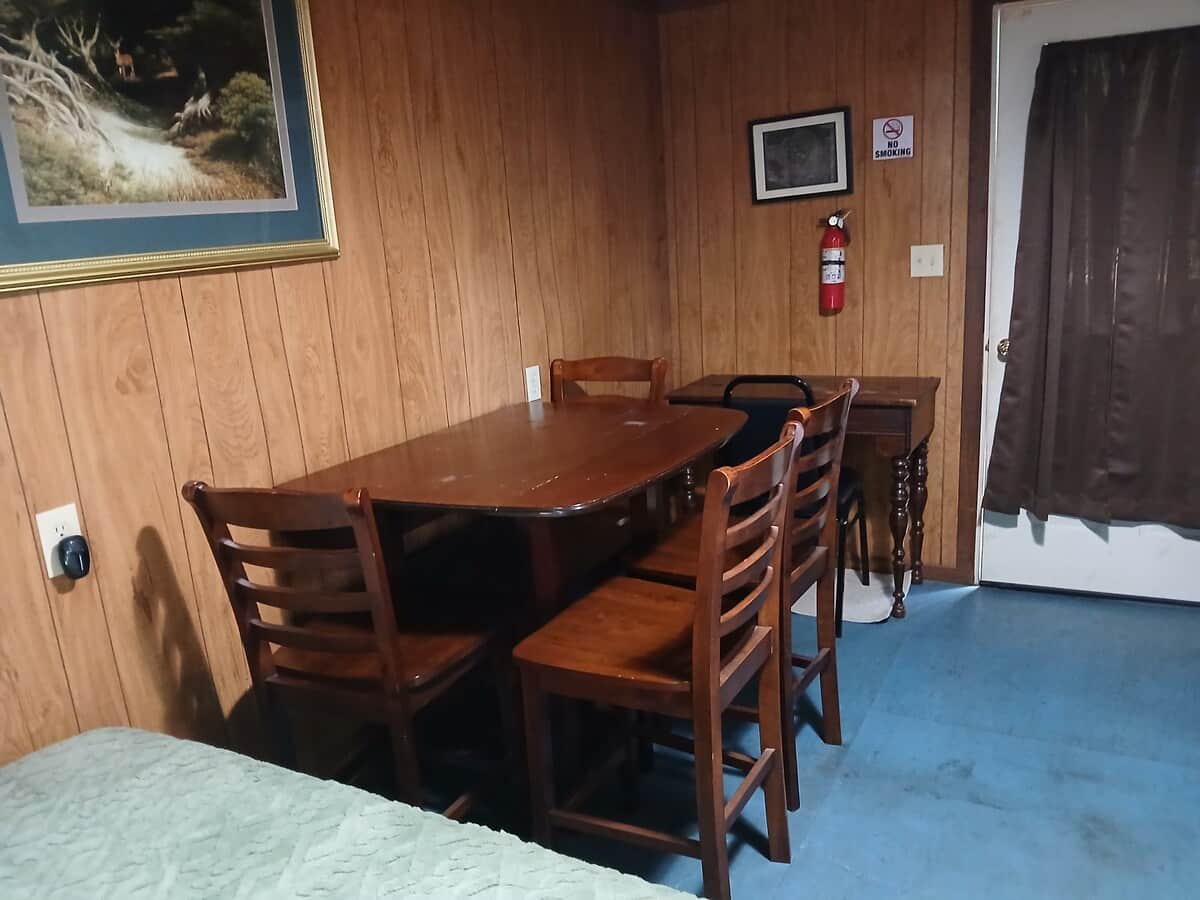 Vacation Rentals in Tennessee: A framed landscape painting above a dining table and chairs in a wood-paneled bunkhouse, with a bed in the foreground.