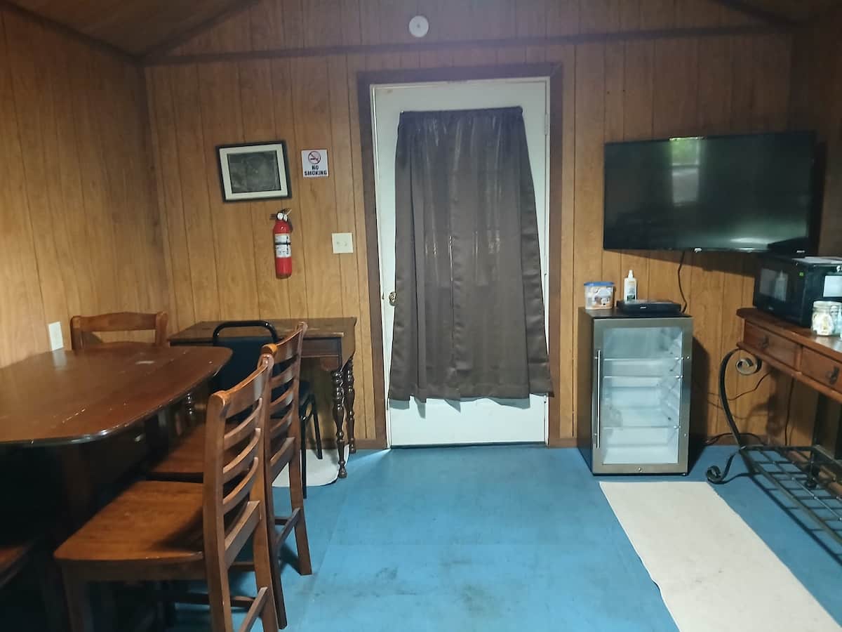 Vacation Rentals in Tennessee: A dining table and ladder-back chairs inside a wood-paneled bunkhouse, with a television on the wall and a mini fridge beside the door.