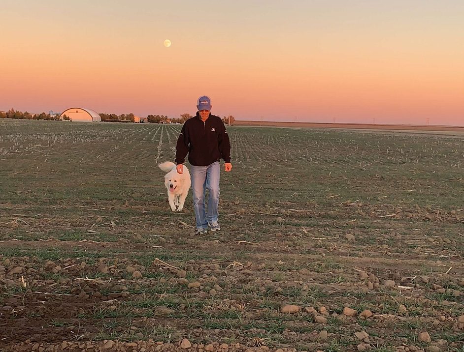 Scott Arthaud walking a field with his dog at sunset