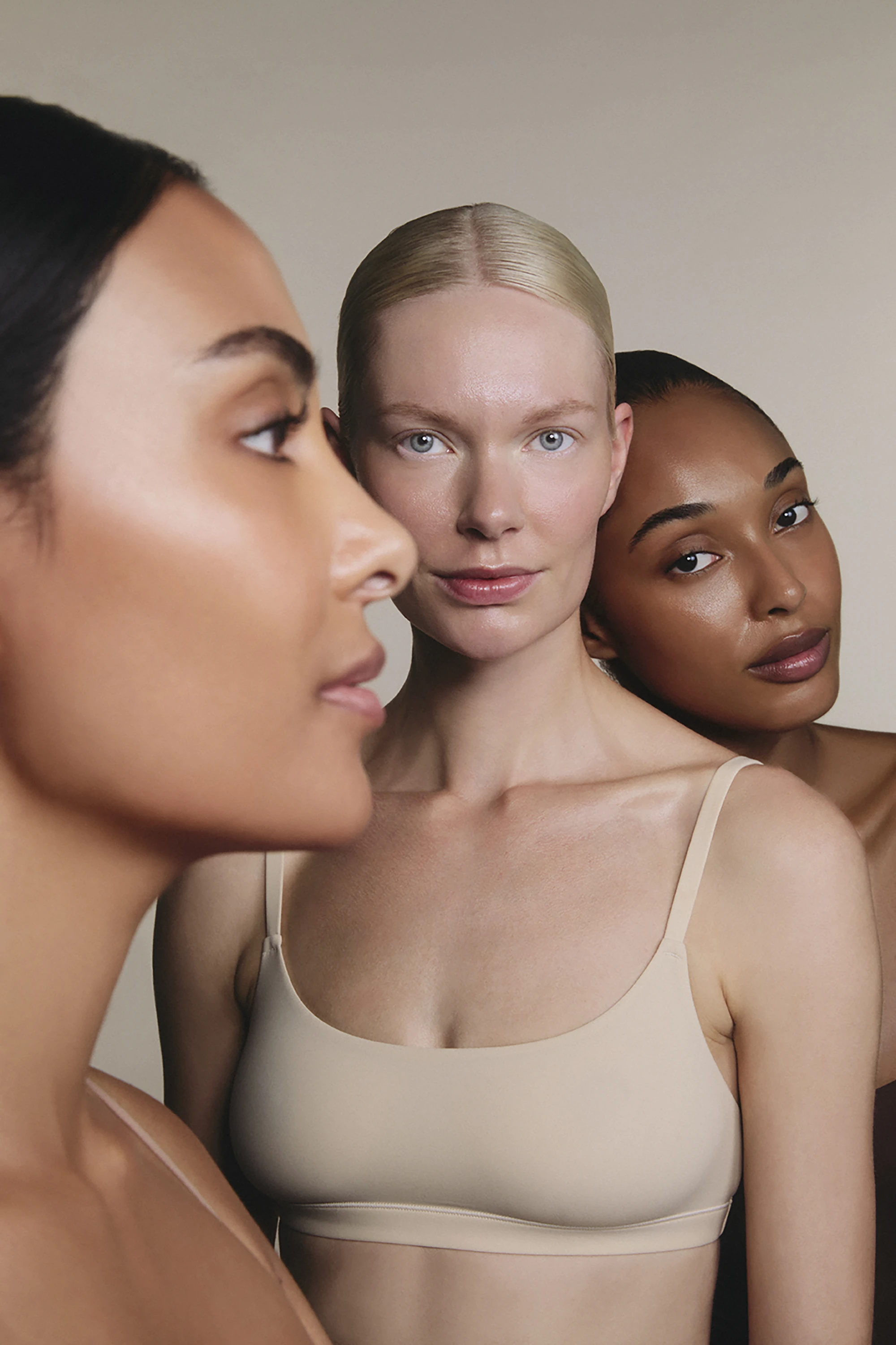 Portrait of three diverse women with natural skin tones wearing neutral-colored tops against a plain background.
