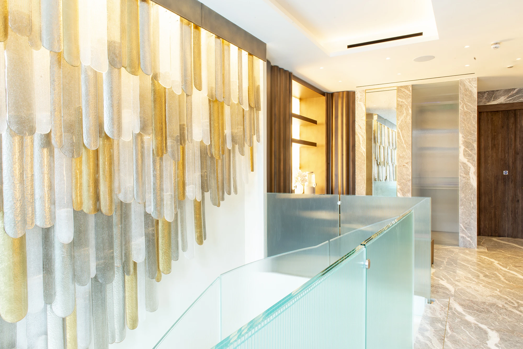 Modern interior with glass railing, marble floor, and gold and silver decorative wall panels.