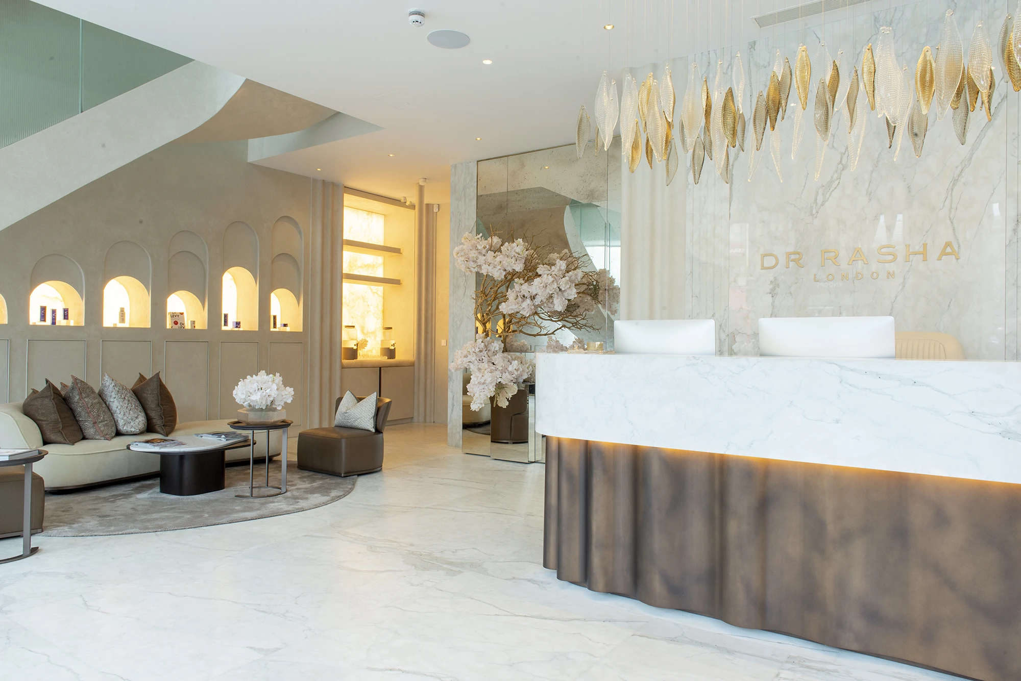Modern clinic reception with marble desk, elegant seating, decorative pillows, and floral arrangement.