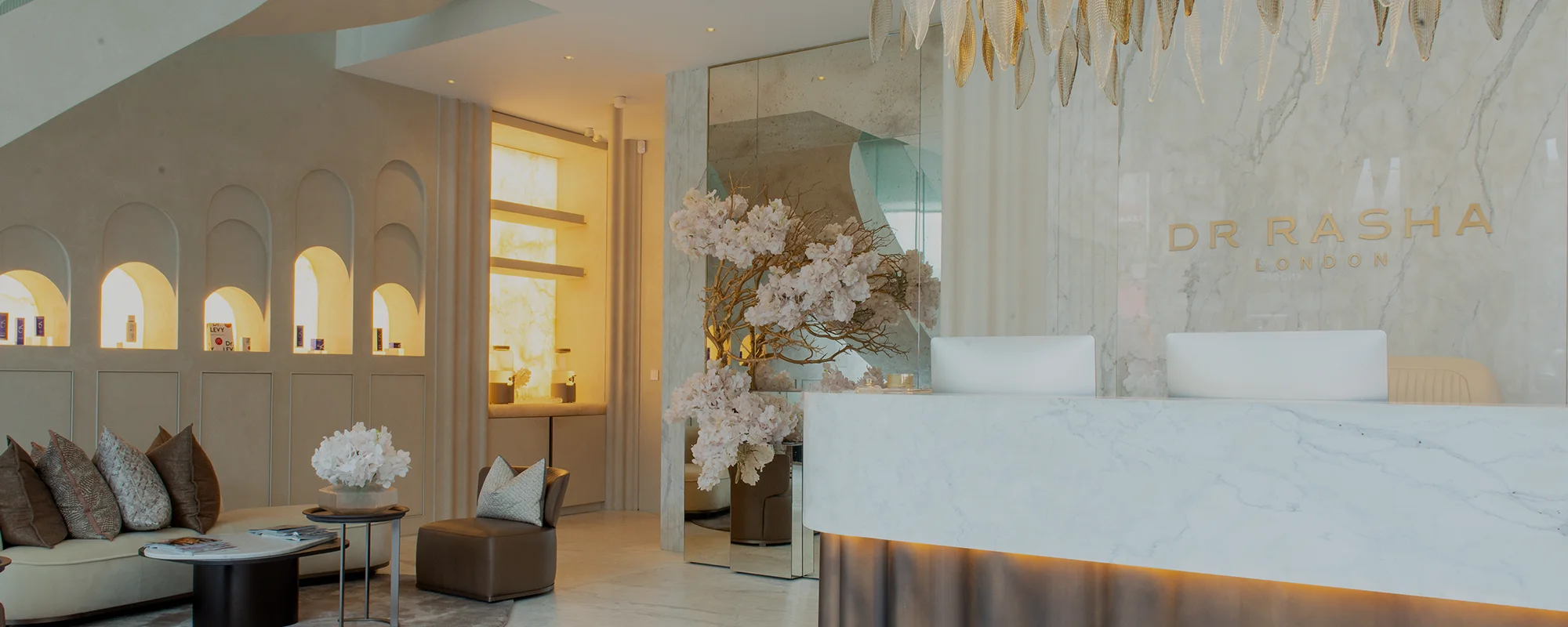 Modern clinic reception with marble desk, white flowers, seating area, and illuminated product niches.