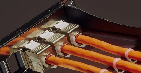 Close-up of several bright orange cables plugged into metallic ports inside a dark electronic device. The cables run parallel across the frame, secured with small white bands.