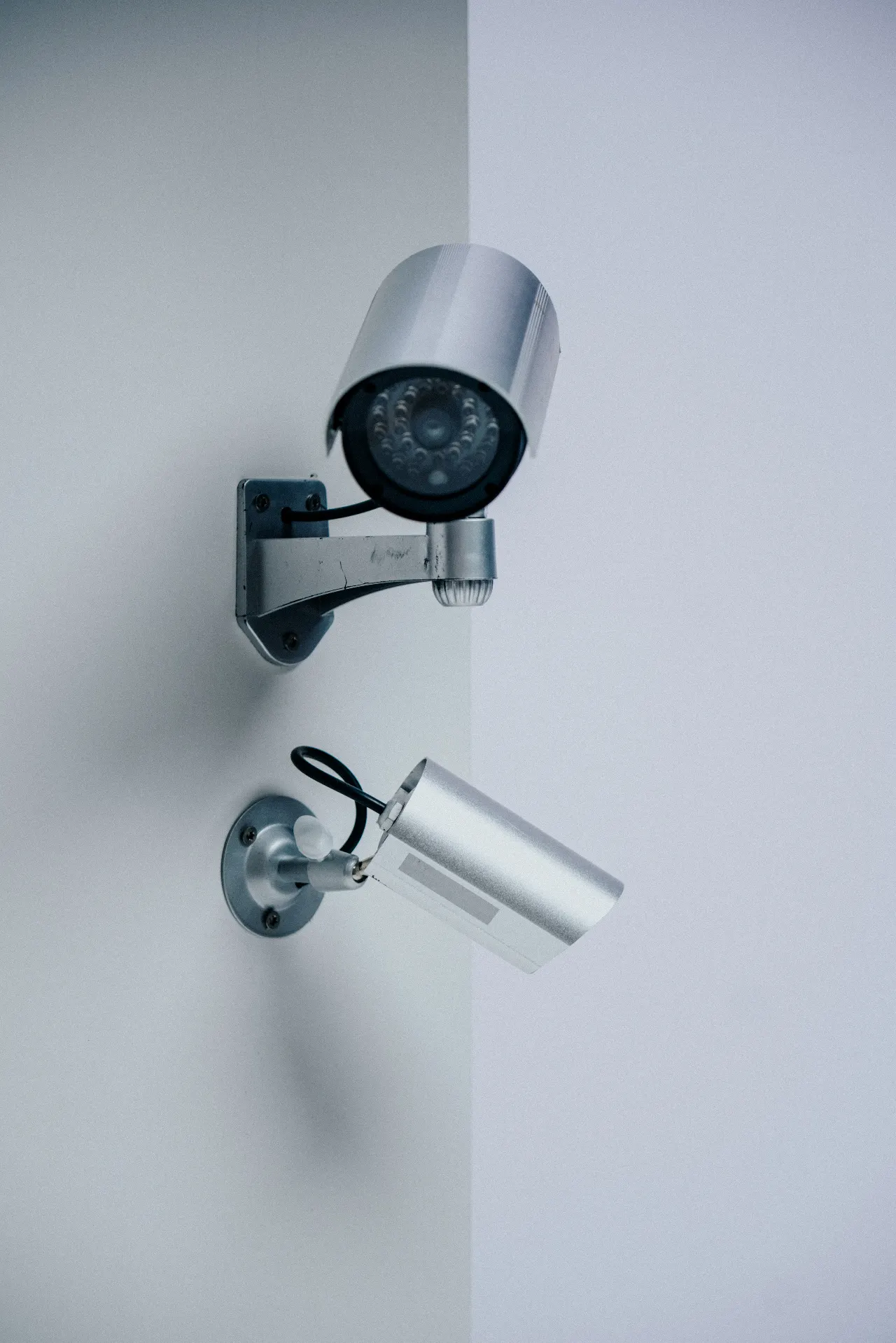 Two silver surveillance cameras mounted on adjacent walls point in different directions.