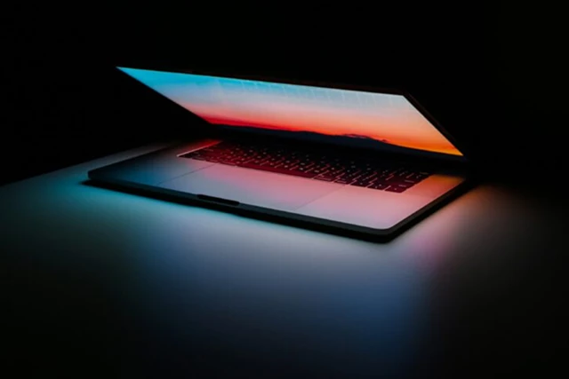 A partially closed laptop glowing in a dark room, its screen casting orange and blue light.