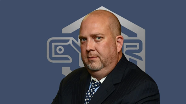 A man with a short beard in a dark pinstripe suit and patterned tie, CYBR logo in the background.