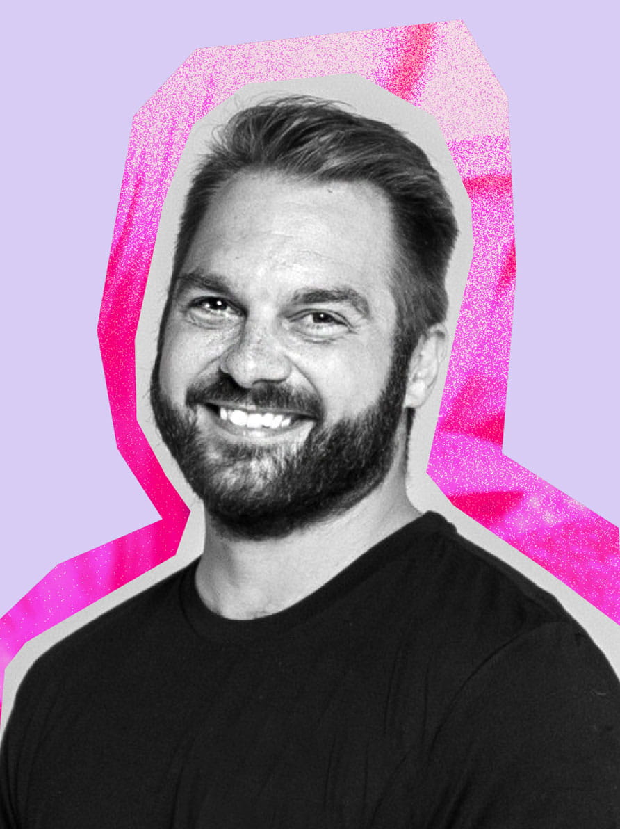Andrew has short hair and a brown beard. He is wearing a black shirt and smiling at the camera.