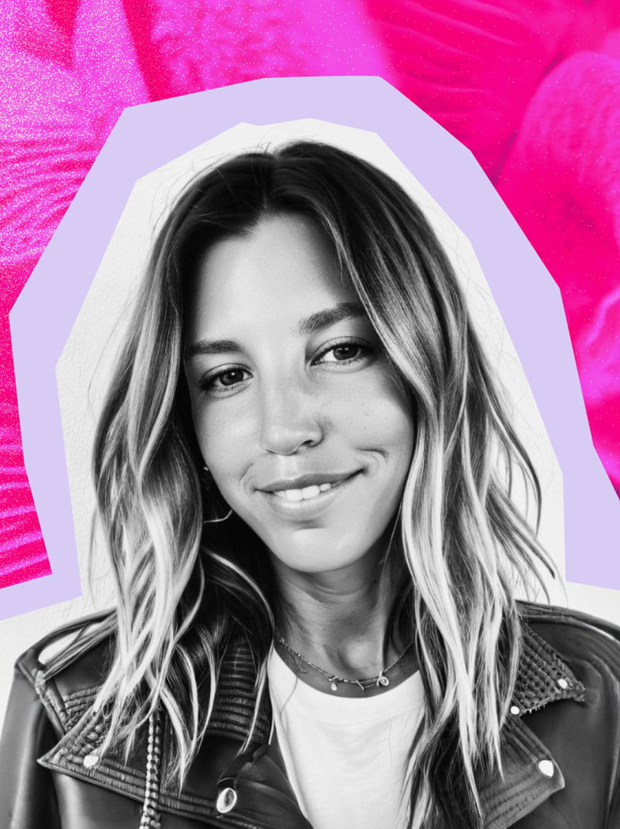 Nikki smiles at the camera. She has long blonde hair and a leather jacket over a white tee.