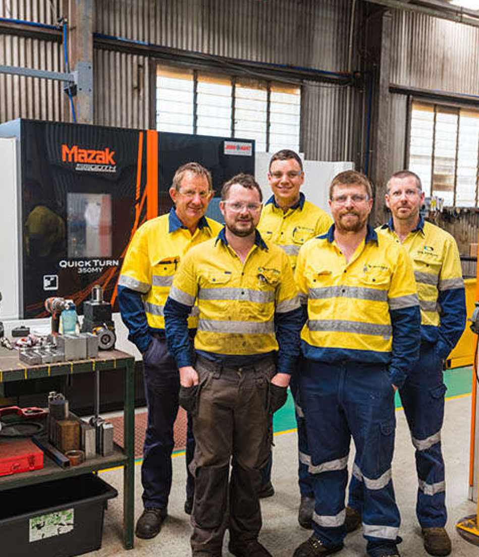 a group of manufacturing workers stand smiling together in their high-vis shirts inside a warehouse.