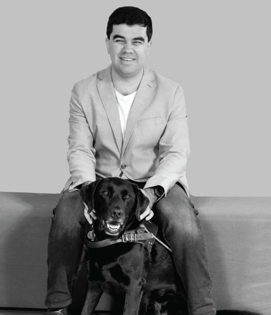 A man in a blazer sits happily with his guide dog.