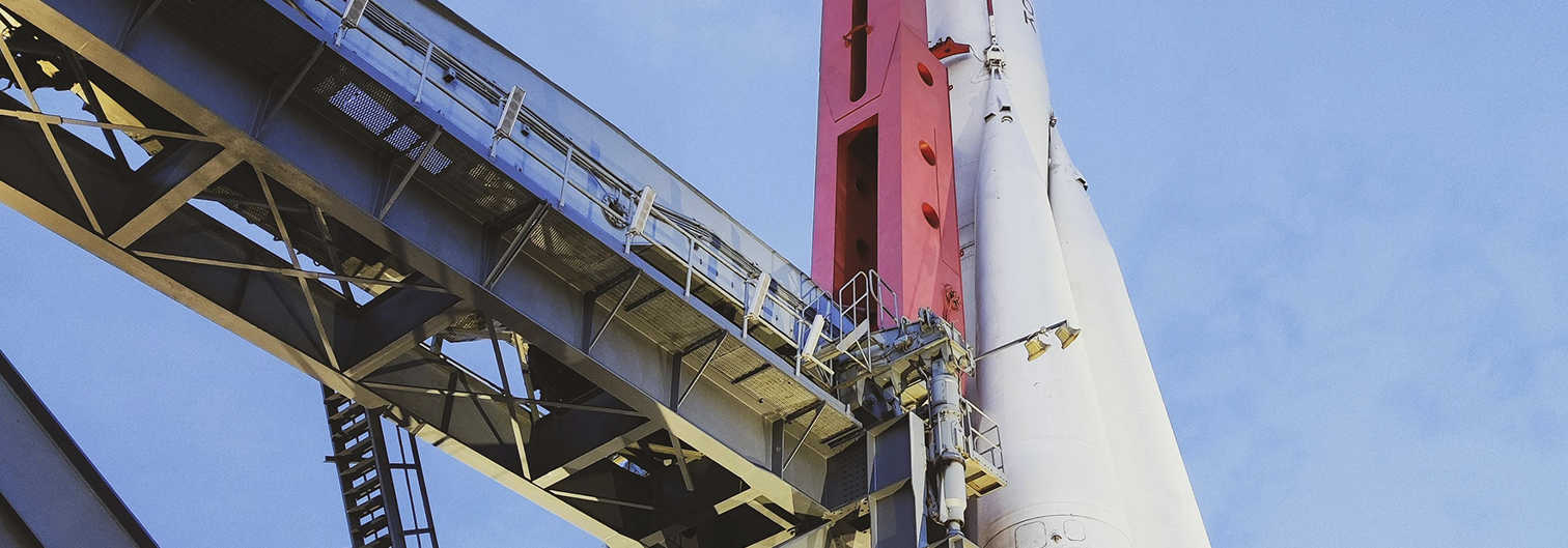 Close-up view of a rocket attached to a launch gantry structure against a blue sky.