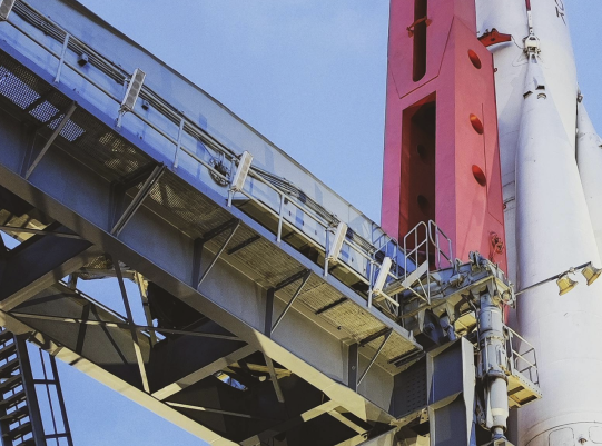 Close-up view of a rocket on a launch pad with metal scaffolding and support structures under a clear blue sky.