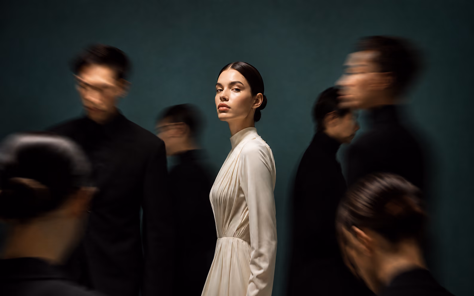 Woman in a pale dress among dark-clothed figures in motion blur