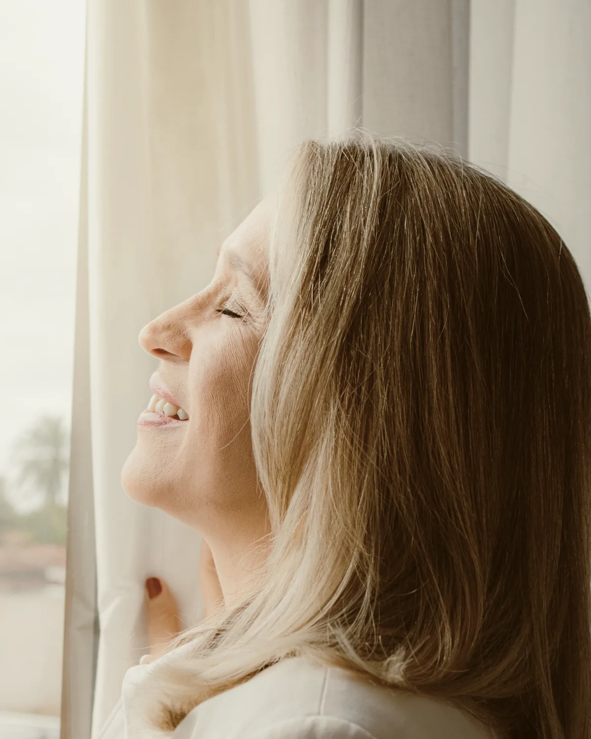 A woman smiling with her eyes closed in soft daylight